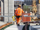 En bantekniker från Infranord i orange skyddskläder som bär på ett verktygt